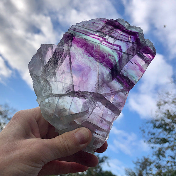 regenboog fluoriet schijf mineralen in de hand tegen het licht houdend