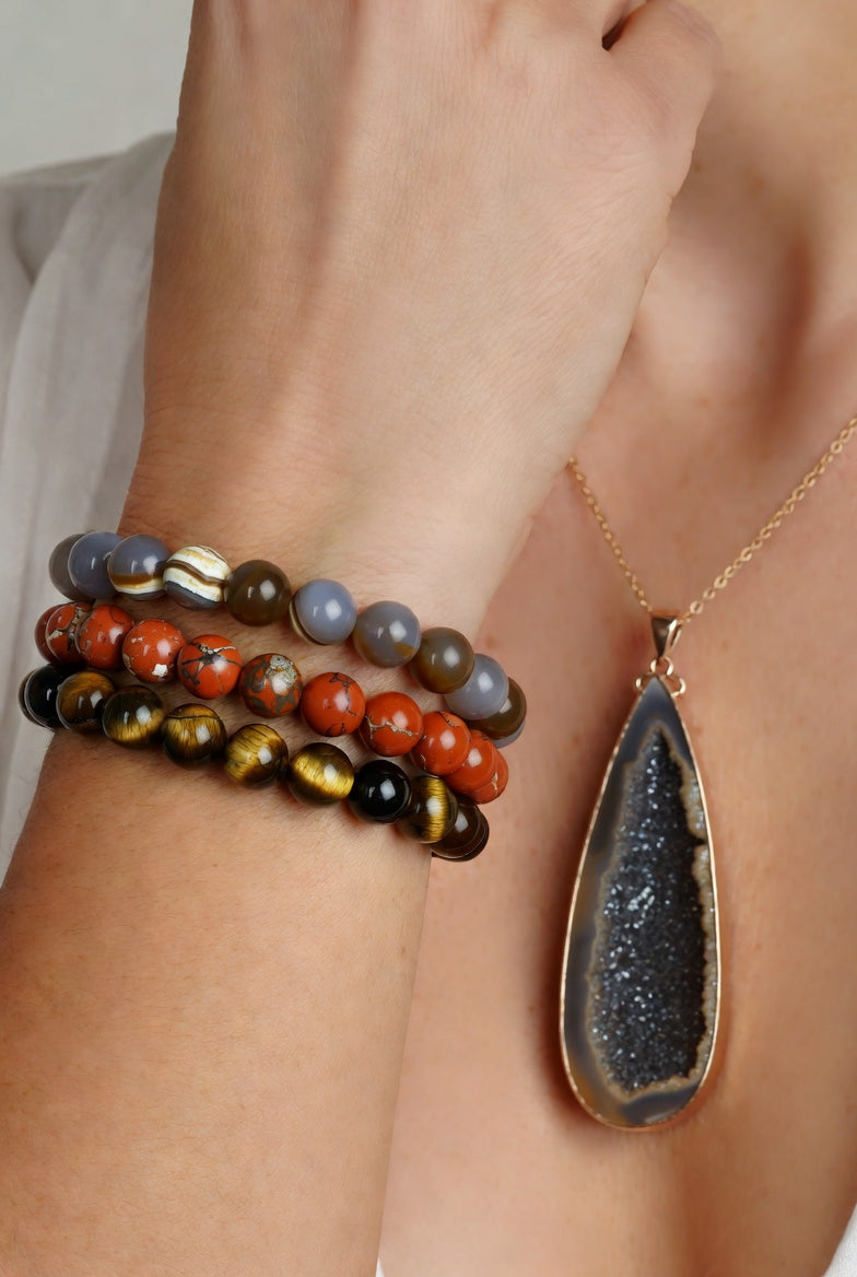 Vrouw draagt stack van 8mm edelstenen armbanden met agaat, jaspis en tijgeroog, gecombineerd met een lange druzy agaat hanger