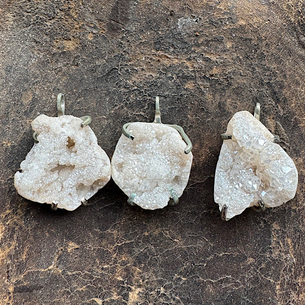 3 bergkristallen hangertjes voor aan een ketting op een ledere ondergrond